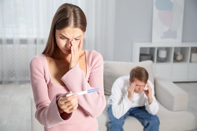 Photo of Worried woman with pregnancy test and her husband at home, selective focus