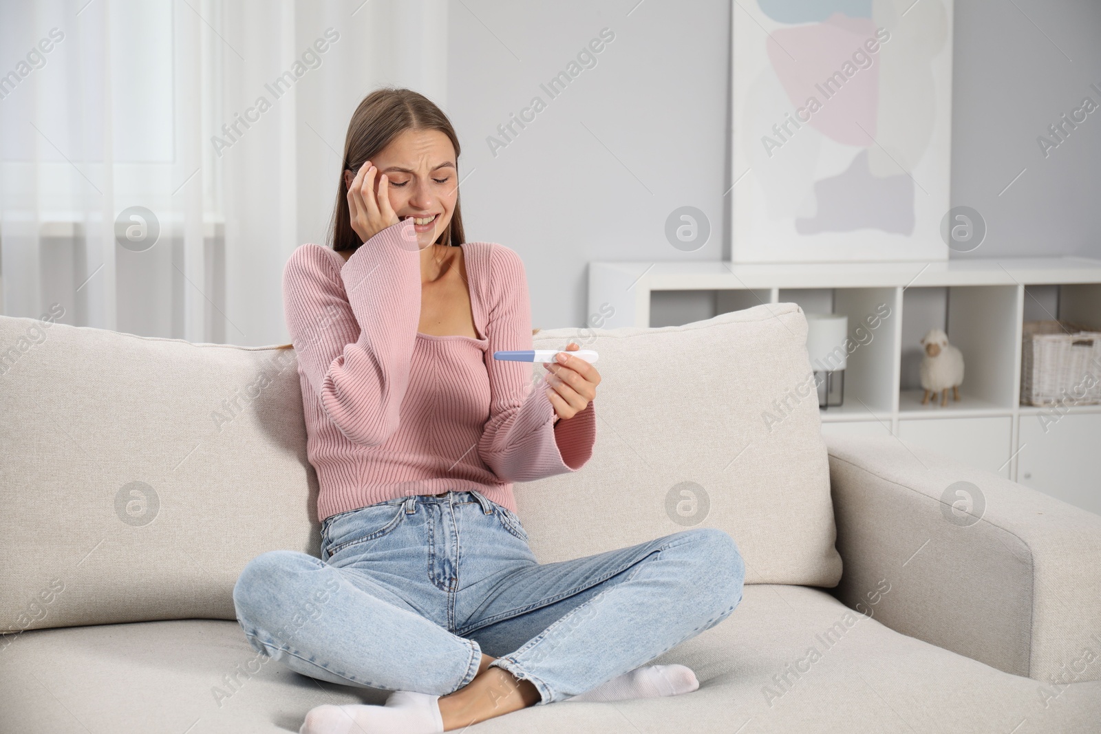 Photo of Happy young woman with pregnancy test on sofa at home