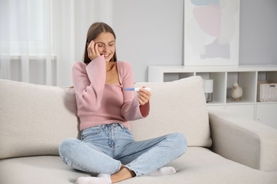 Photo of Happy young woman with pregnancy test on sofa at home