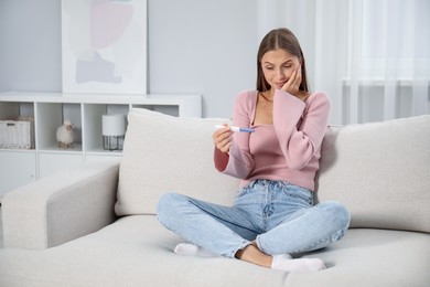 Photo of Emotional young woman with pregnancy test on sofa at home