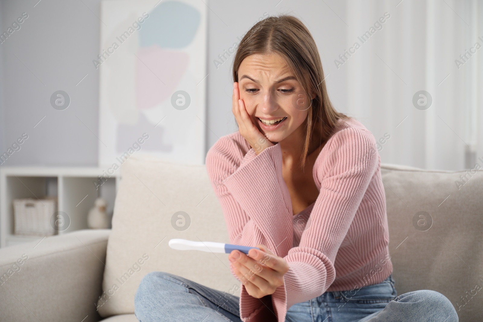 Emotional young woman with pregnancy test on sofa at home Photo of Emotional young woman with pregnancy test on sofa at home
