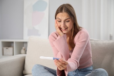 Photo of Emotional young woman with pregnancy test on sofa at home