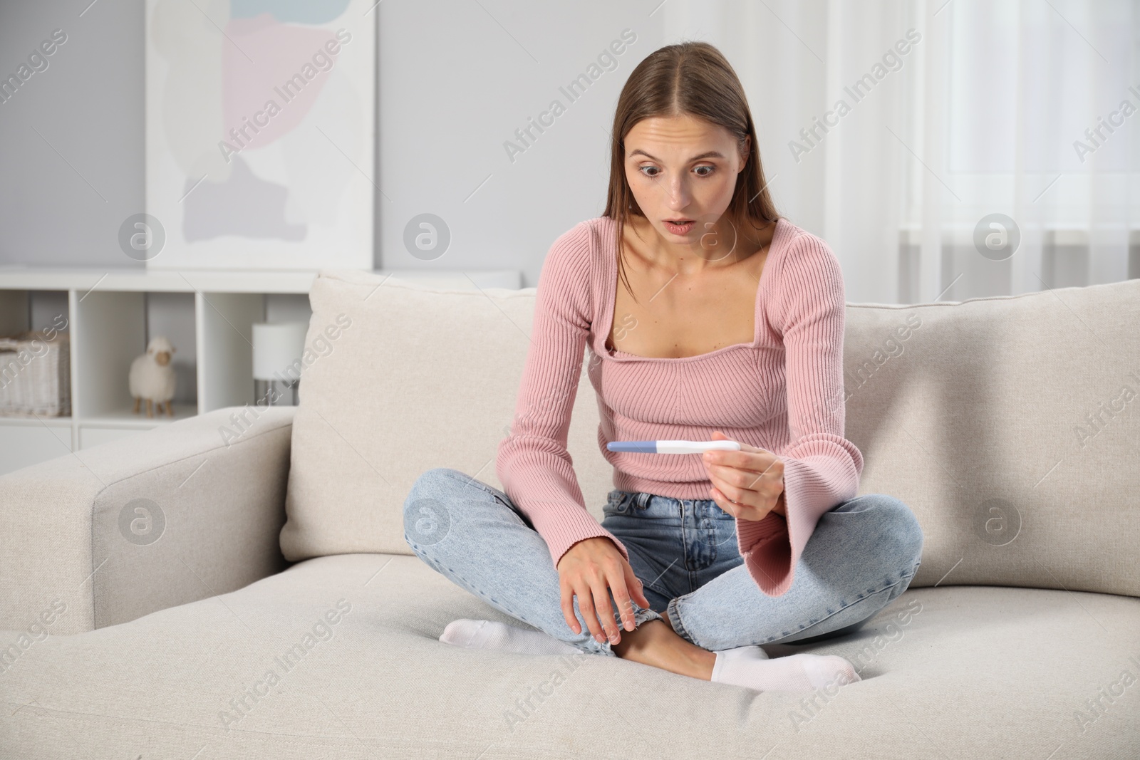 Emotional young woman with pregnancy test on sofa at home Photo of Emotional young woman with pregnancy test on sofa at home
