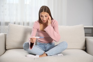 Photo of Emotional young woman with pregnancy test on sofa at home