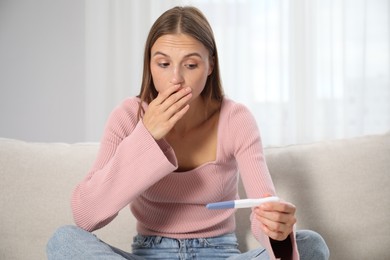 Photo of Emotional young woman with pregnancy test on sofa at home