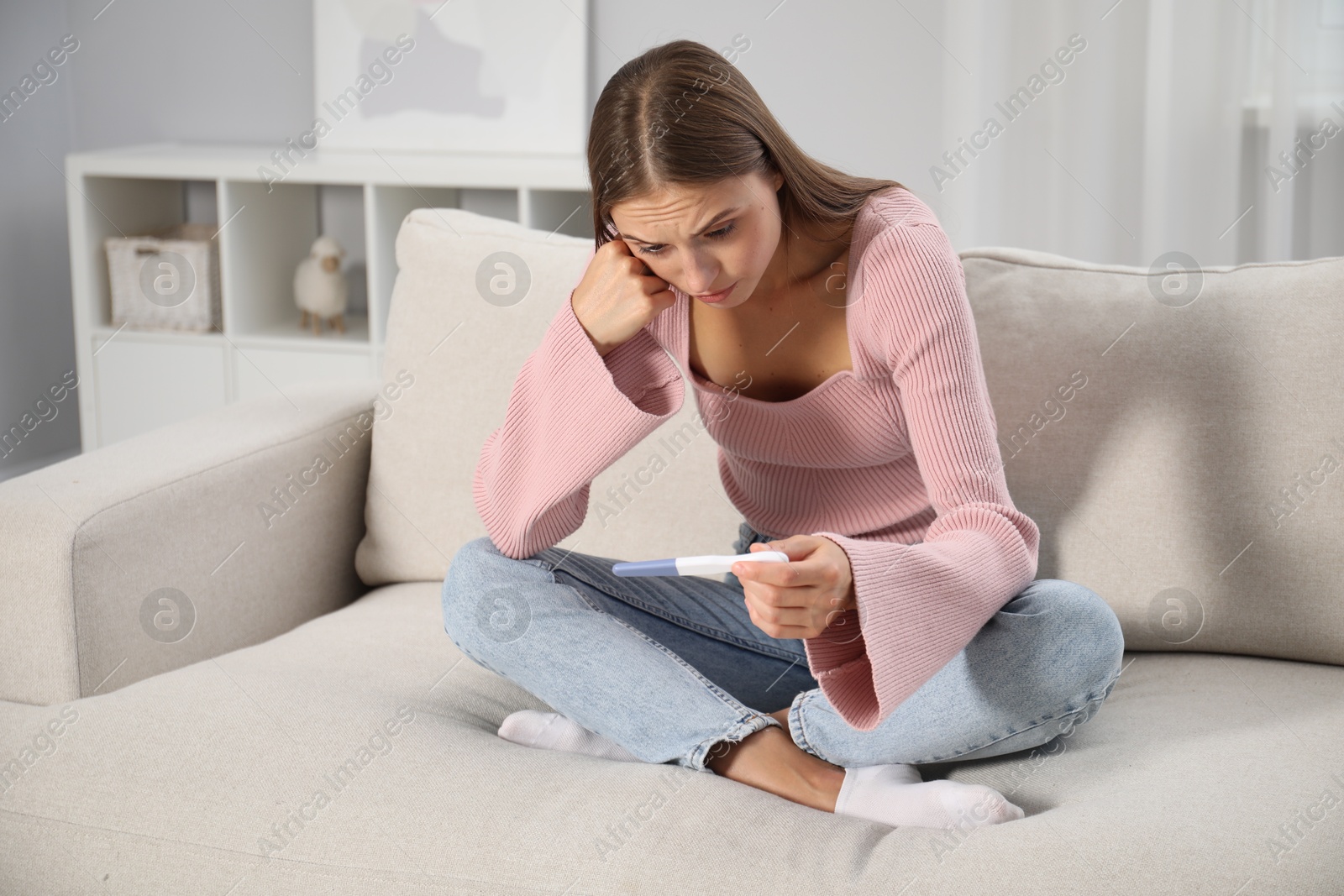 Emotional young woman with pregnancy test on sofa at home Photo of Emotional young woman with pregnancy test on sofa at home