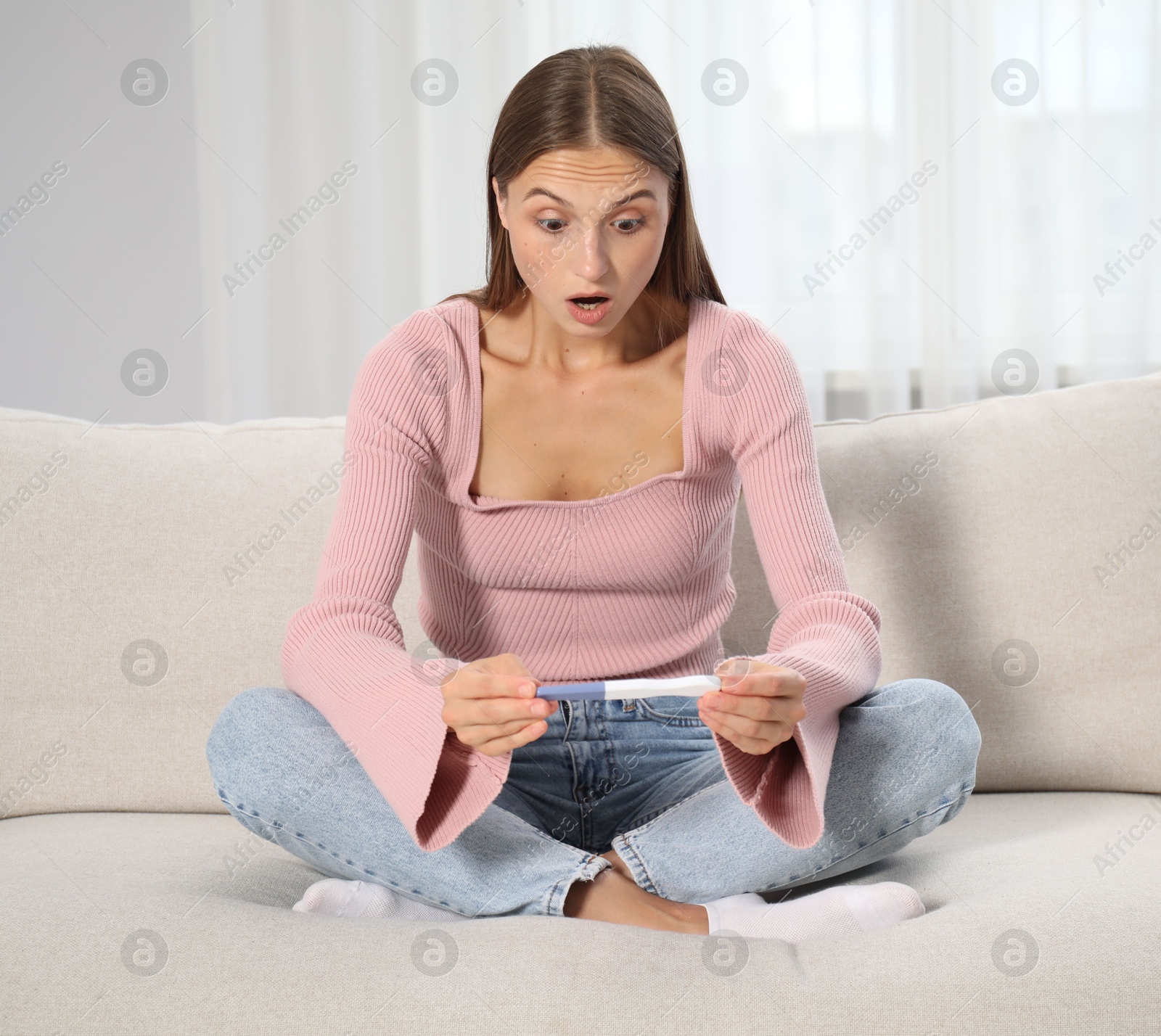 Emotional young woman with pregnancy test on sofa at home Photo of Emotional young woman with pregnancy test on sofa at home