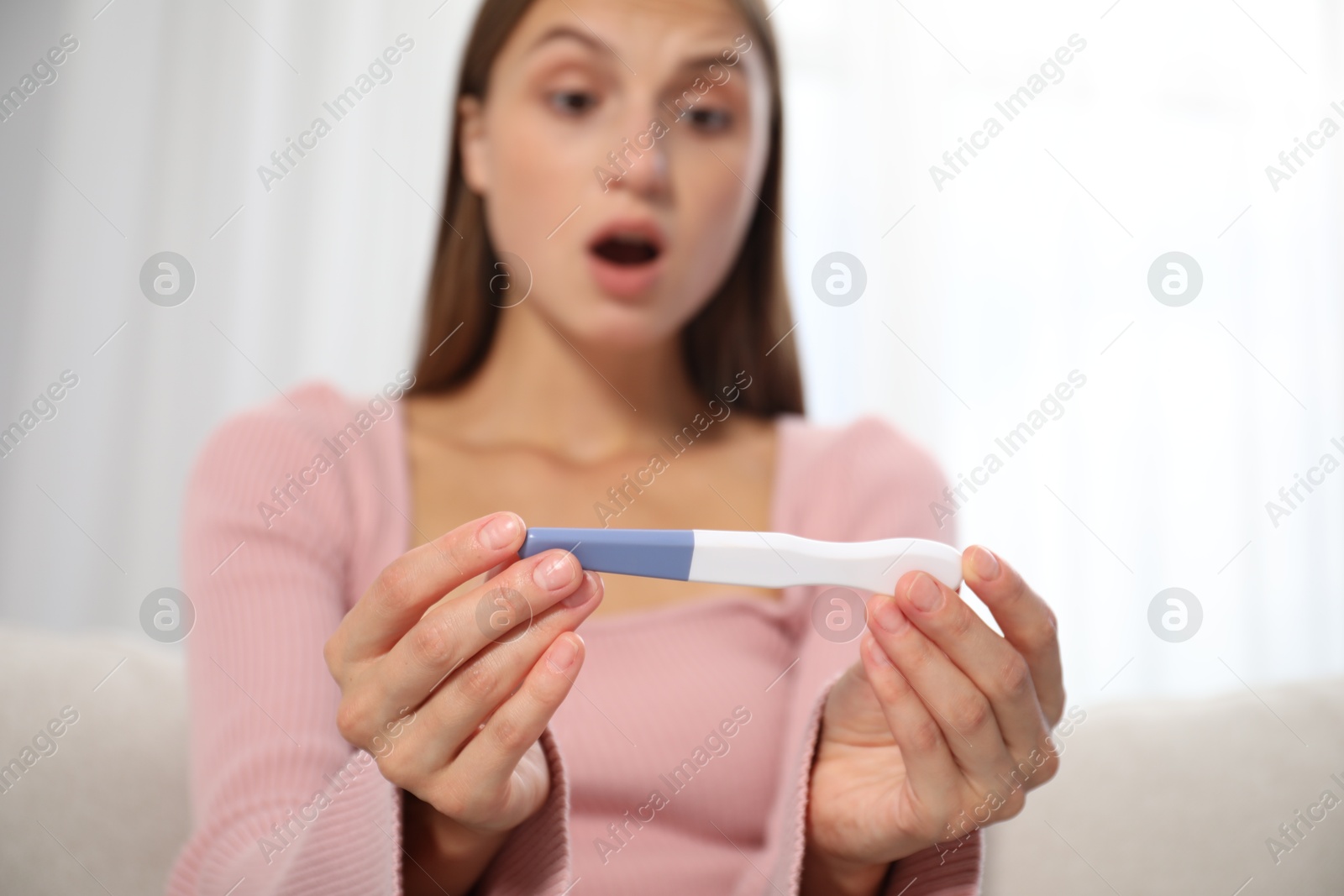 Emotional young woman with pregnancy test indoors, selective focus Photo of Emotional young woman with pregnancy test indoors, selective focus