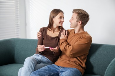 Photo of Happy couple with pregnancy test on sofa at home