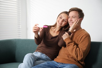 Photo of Happy couple with pregnancy test on sofa at home