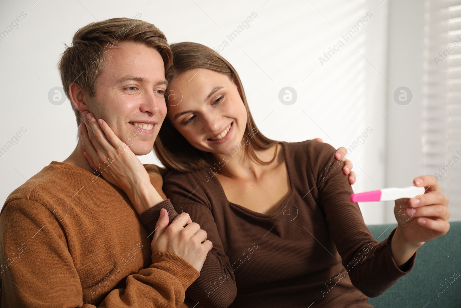 Happy couple with pregnancy test on sofa at home Photo of Happy couple with pregnancy test on sofa at home