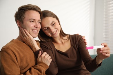 Photo of Happy couple with pregnancy test on sofa at home