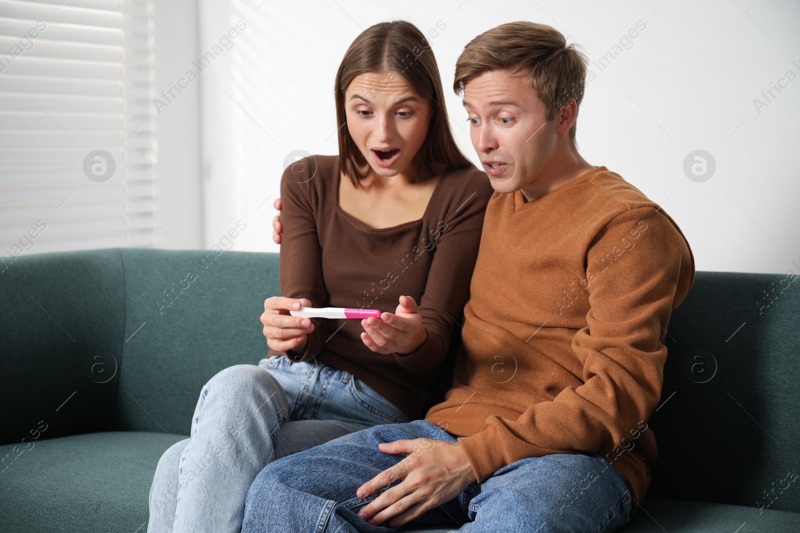 Photo of Emotional couple with pregnancy test on sofa at home