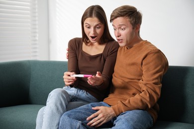 Photo of Emotional couple with pregnancy test on sofa at home