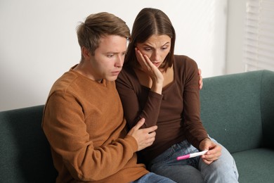 Photo of Worried couple with pregnancy test on sofa at home