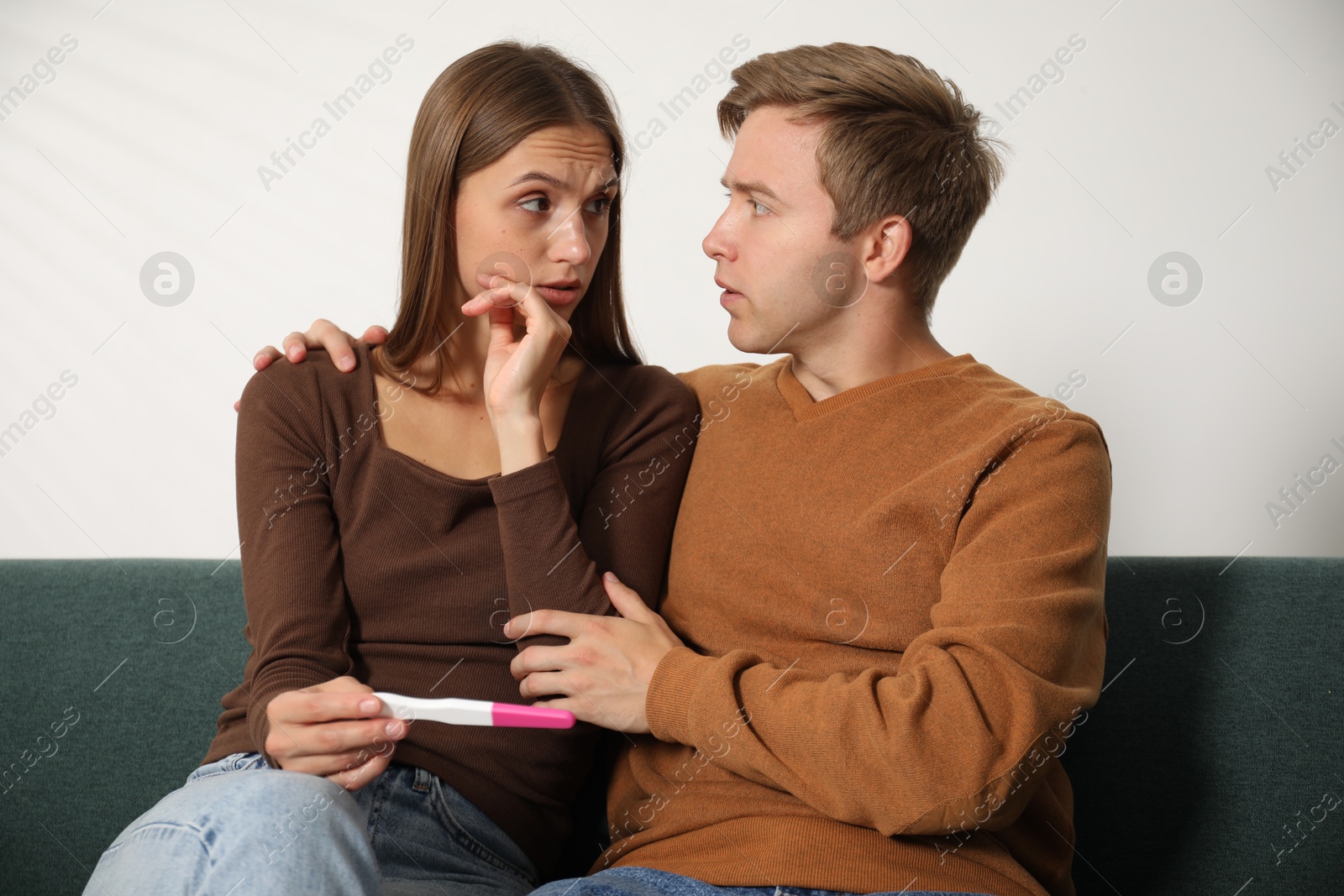Worried couple with pregnancy test on sofa at home Photo of Worried couple with pregnancy test on sofa at home