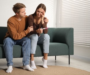 Photo of Worried couple with pregnancy test on sofa at home