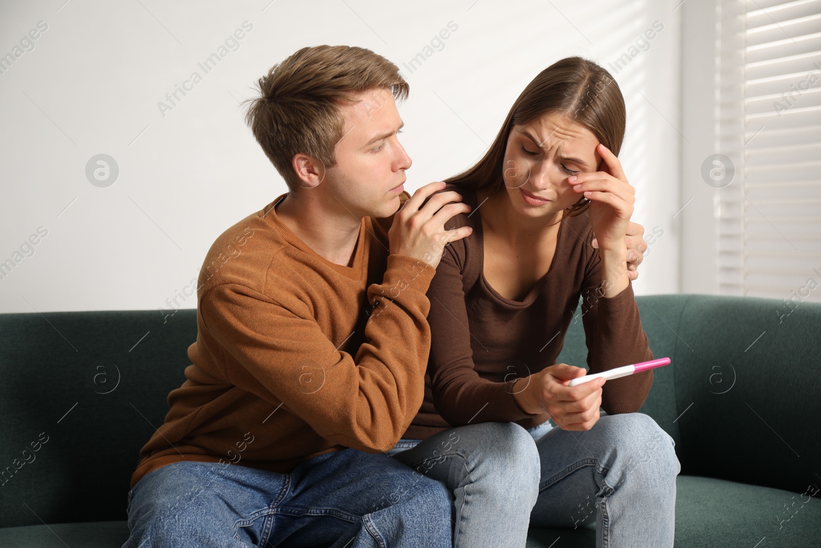 Photo of Worried couple with pregnancy test on sofa at home