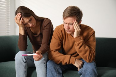 Photo of Worried couple with pregnancy test on sofa at home
