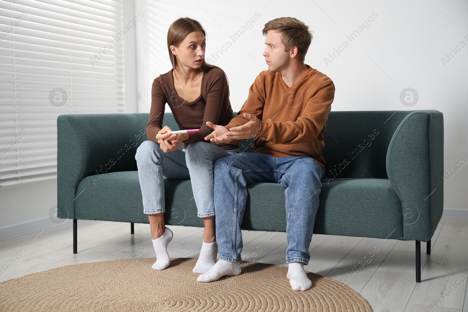Photo of Worried couple with pregnancy test on sofa at home