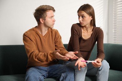 Photo of Worried couple with pregnancy test on sofa at home