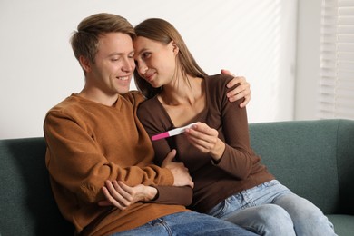 Photo of Happy couple with pregnancy test on sofa at home