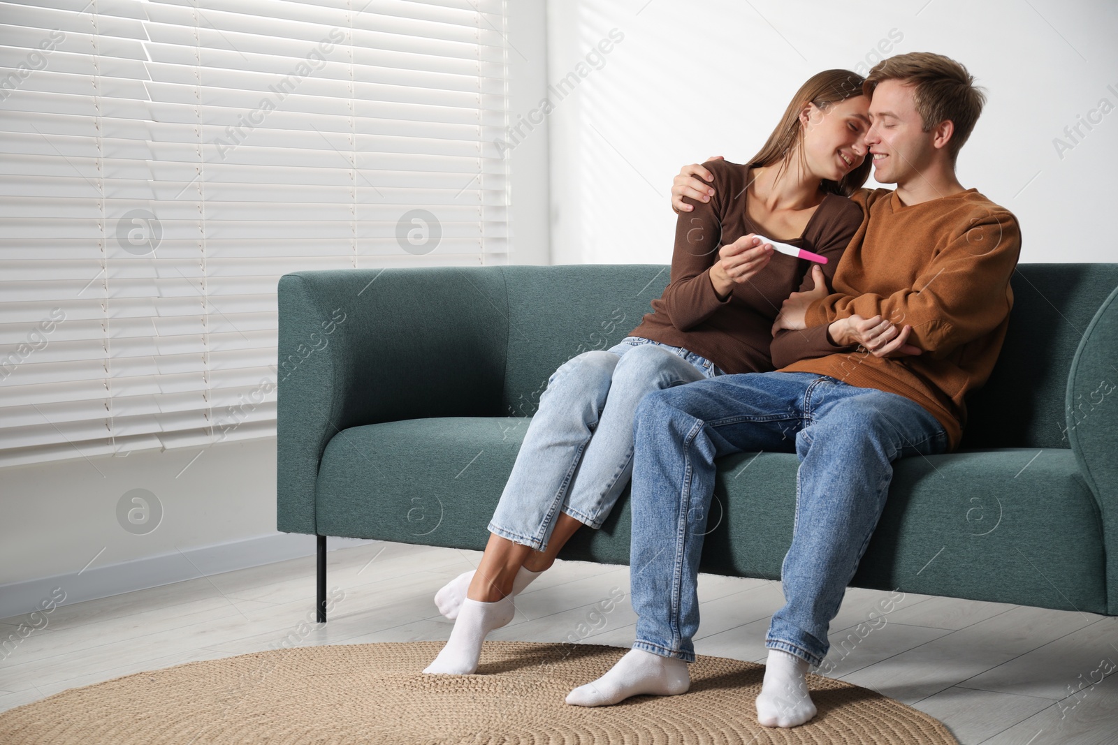 Happy couple with pregnancy test on sofa at home Photo of Happy couple with pregnancy test on sofa at home