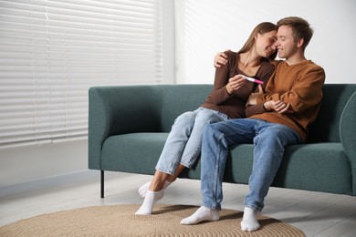 Photo of Happy couple with pregnancy test on sofa at home