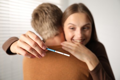 Photo of Happy couple with pregnancy test at home, selective focus