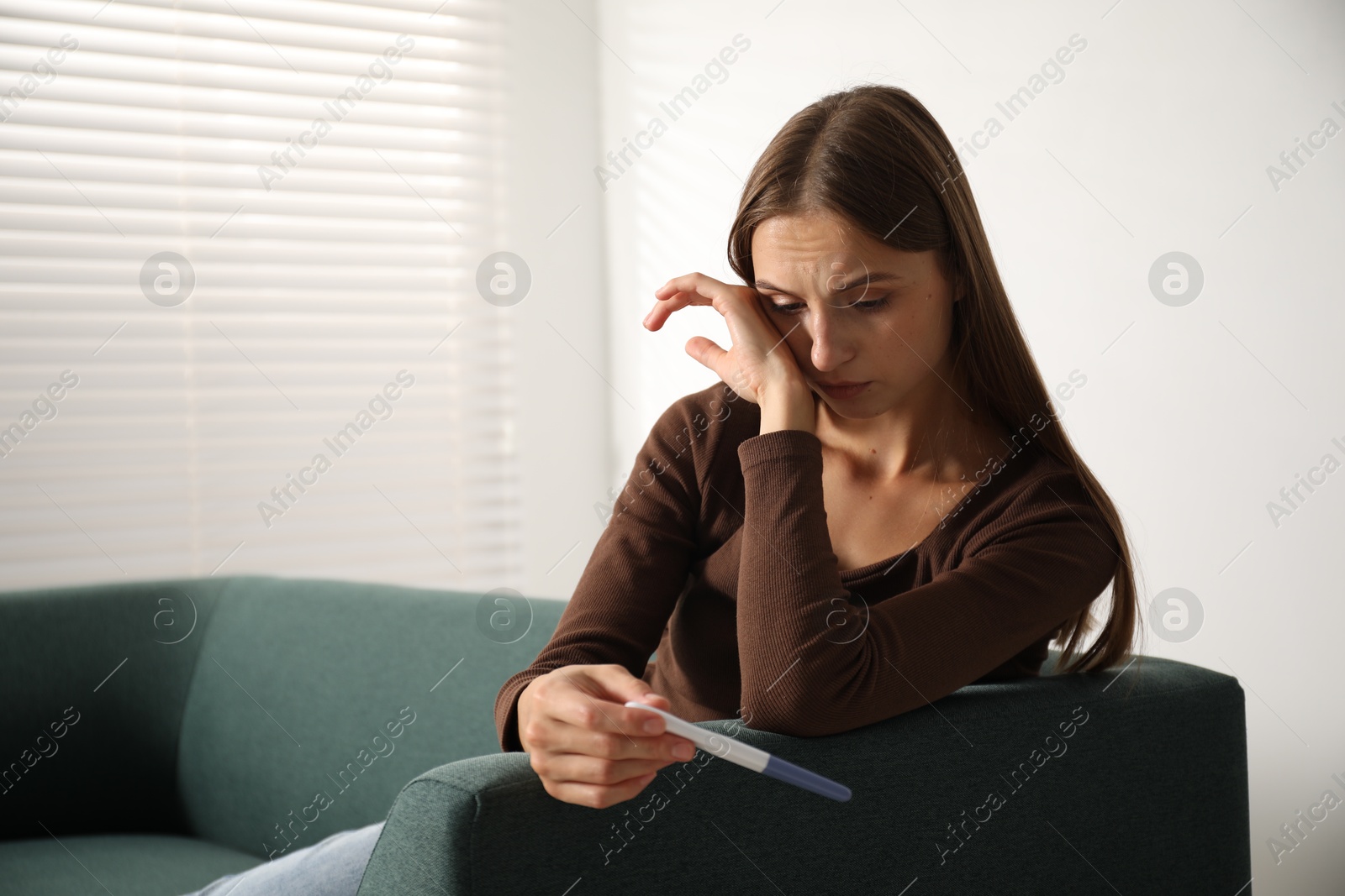 Photo of Upset young woman with pregnancy test on sofa at home, space for text