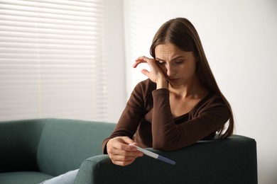 Photo of Upset young woman with pregnancy test on sofa at home, space for text