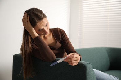 Photo of Upset young woman with pregnancy test on sofa at home, space for text