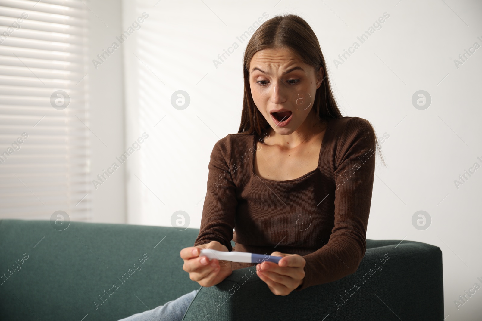 Photo of Emotional young woman with pregnancy test on sofa at home, space for text