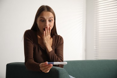 Photo of Emotional young woman with pregnancy test on sofa at home, space for text