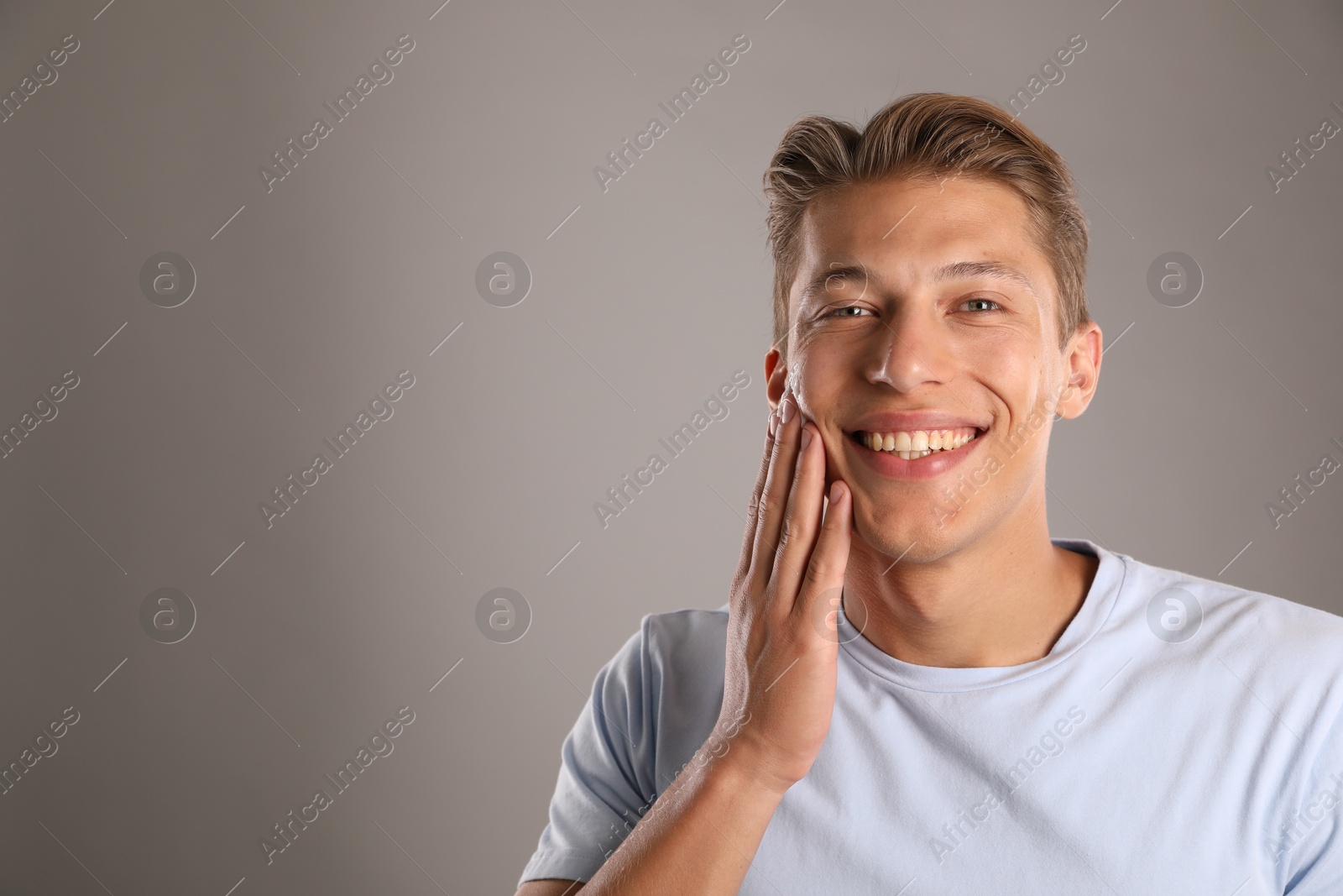Photo of Handsome young man applying cream onto his face on grey background, space for text