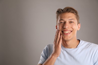 Photo of Handsome young man applying cream onto his face on grey background, space for text