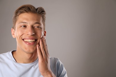 Photo of Handsome young man applying cream onto his face on grey background, space for text