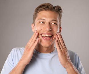 Photo of Handsome young man applying cream onto his face on grey background