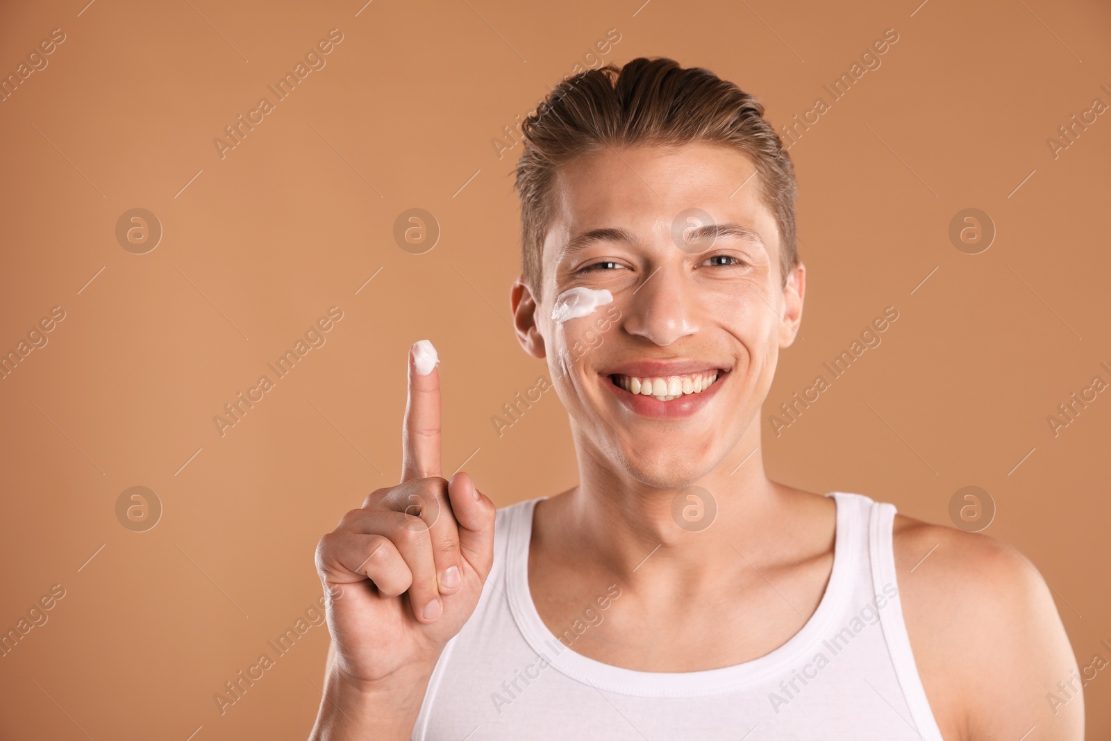 Photo of Handsome young man with cream on his face and finger against light brown background
