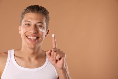 Photo of Handsome young man with cream on his face and finger against light brown background, space for text