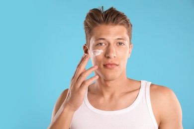 Photo of Handsome young man applying cream onto his face on light blue background