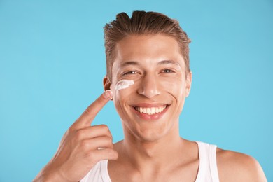 Photo of Handsome young man applying cream onto his face on light blue background
