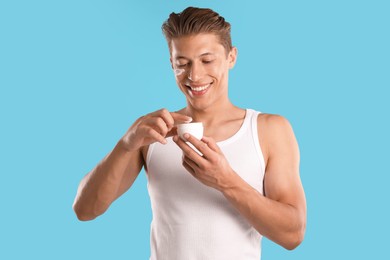 Photo of Handsome young man with jar of face cream on light blue background