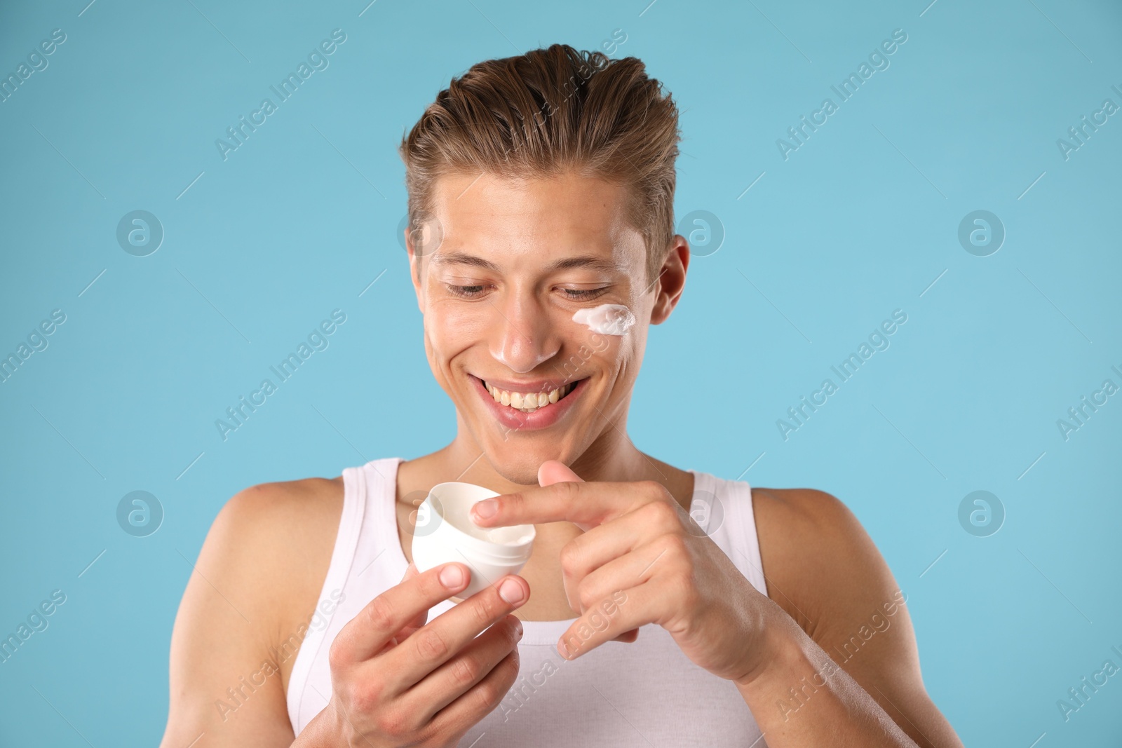 Photo of Handsome young man with jar of face cream on light blue background