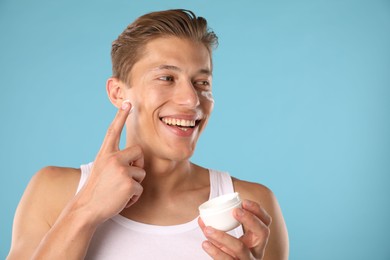 Photo of Handsome young man applying cream onto his face on light blue background