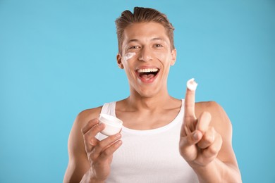 Photo of Handsome young man with jar of face cream on light blue background