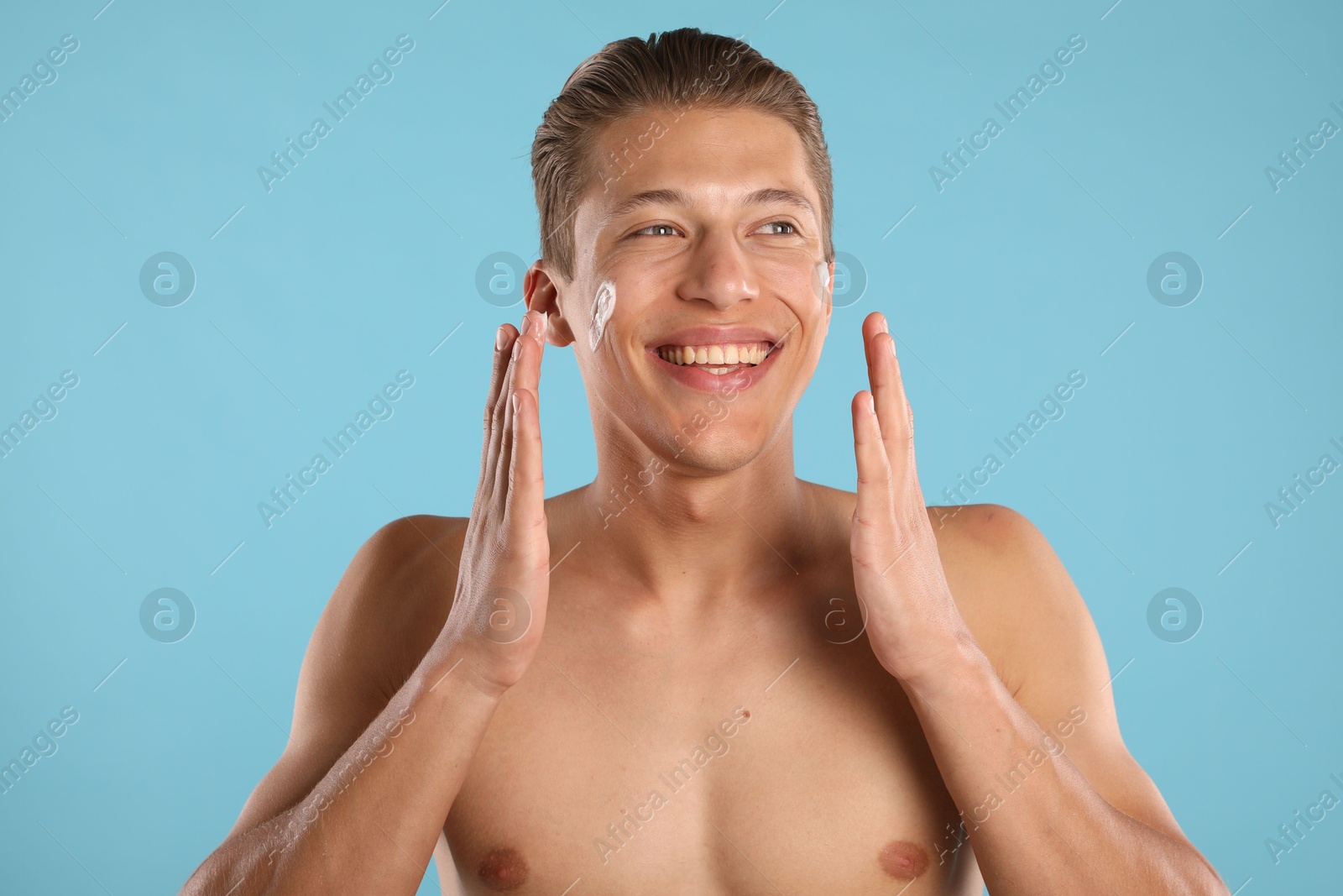 Photo of Handsome young man with cream on his face against light blue background