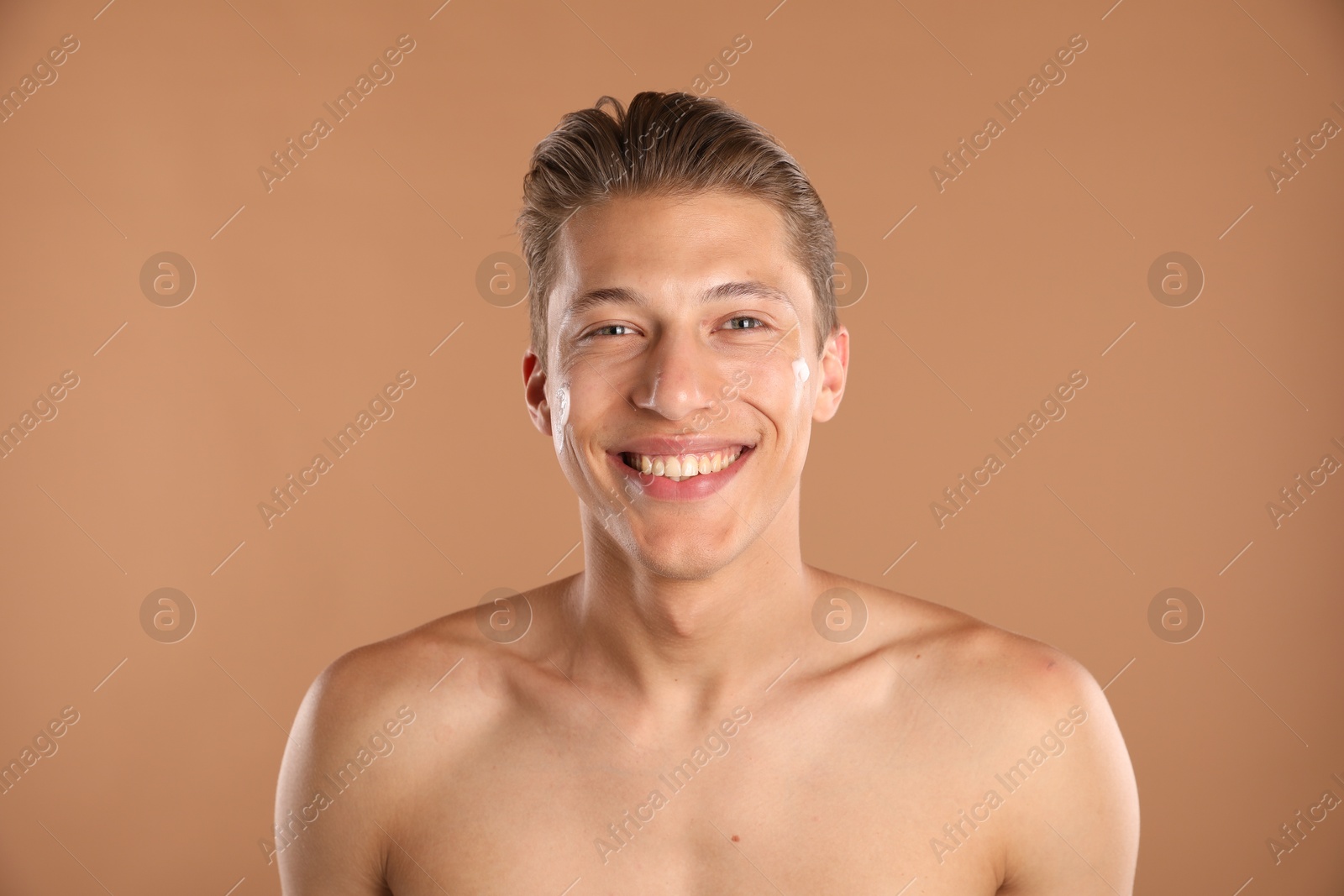 Photo of Handsome young man with cream on his face against light brown background