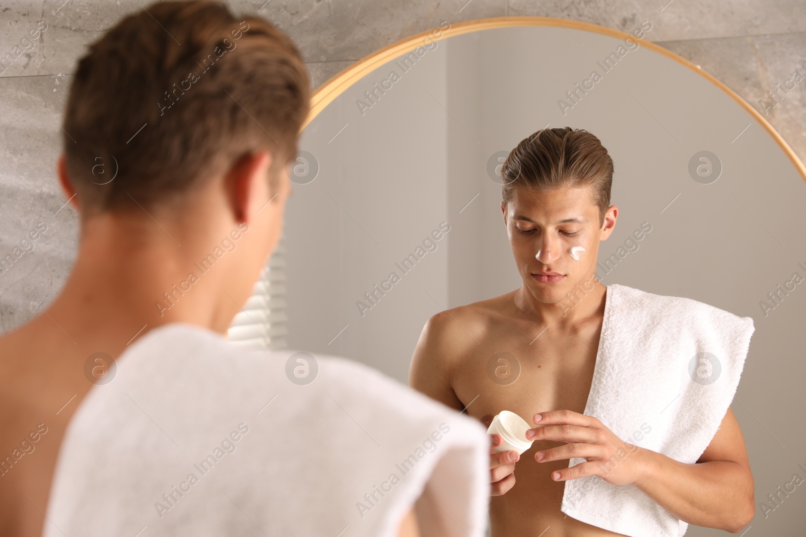 Photo of Handsome young man with jar of face cream near mirror in bathroom
