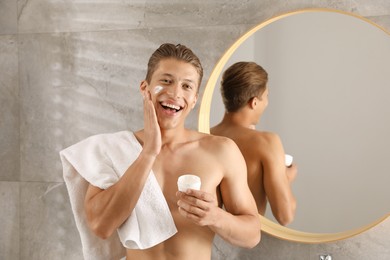Photo of Handsome young man applying cream onto his face in bathroom